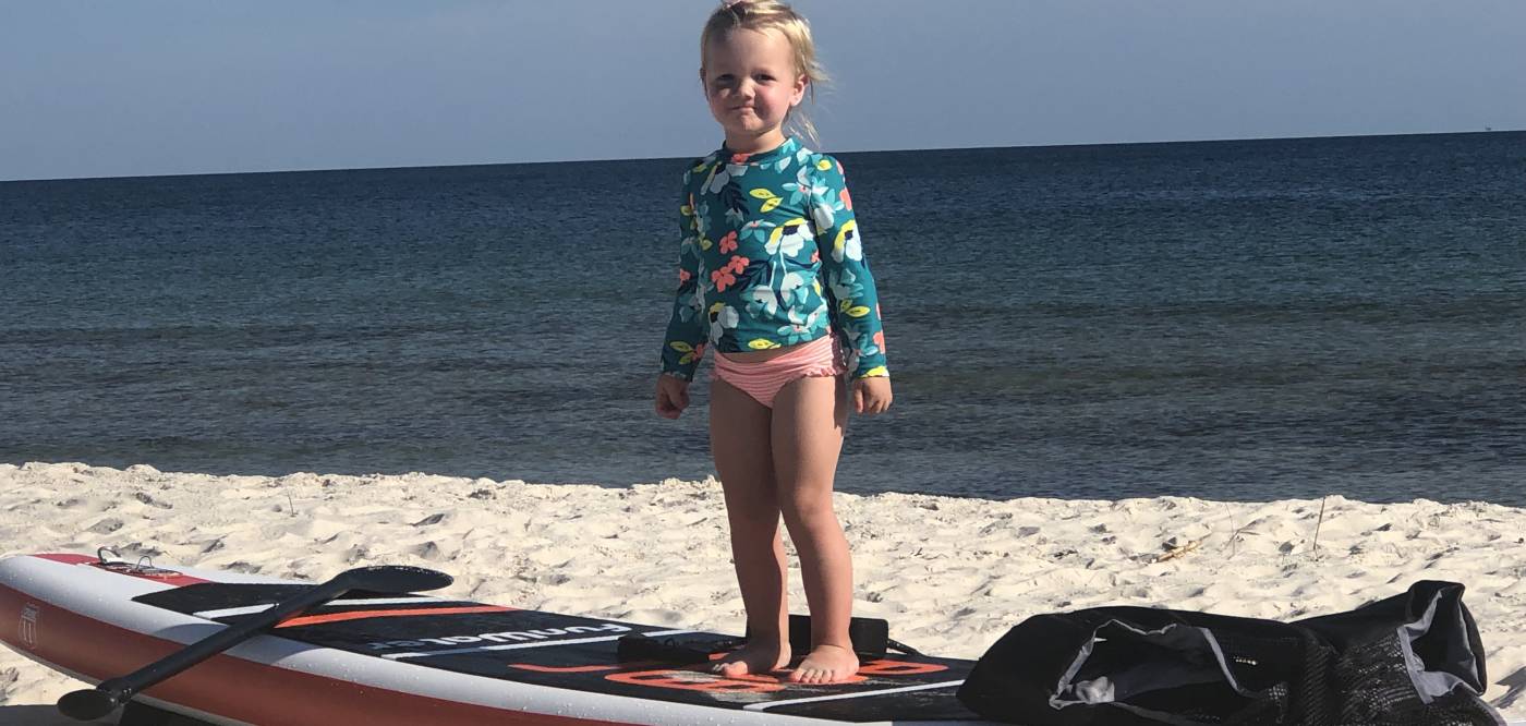 Cute little girl standing on a paddle board in the sand.